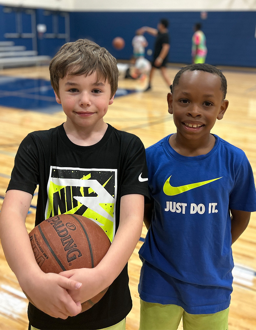 Two boys in a gym. The boy on the left is holding a basketball.