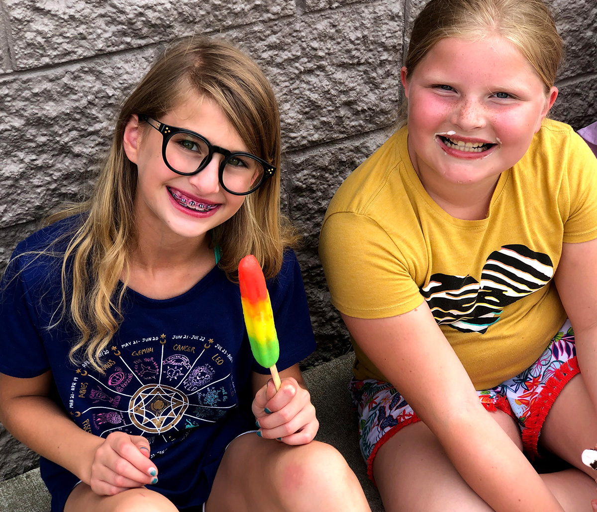 Two kids outside. One is eating a popsicle.